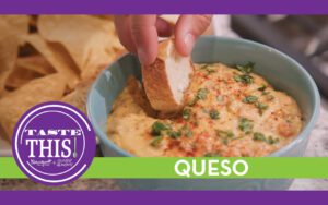 A close-up image of a warm bowl of loaded queso, creamy and rich, featuring a mix of melted cheeses, sautéed onions, and red bell peppers. The queso is topped with fresh cilantro and a sprinkle of smoked paprika. The bowl is surrounded by a mini baguette and tortilla chips, ready for dipping, all set on a countertop.