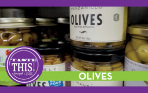 Close-up of jars of green olives on a store shelf with a “Taste This” badge and a green banner labeled “Olives."